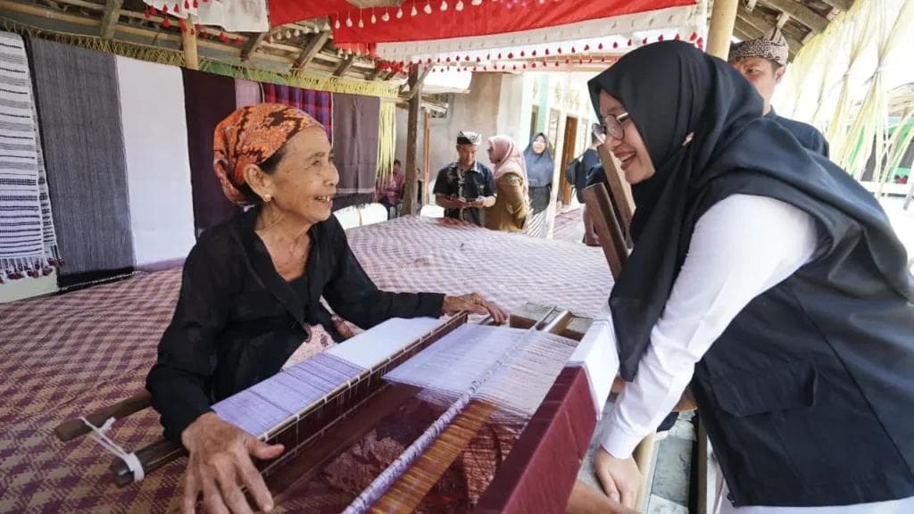 Pengrajin tenun tradisional sedang menenun kain.