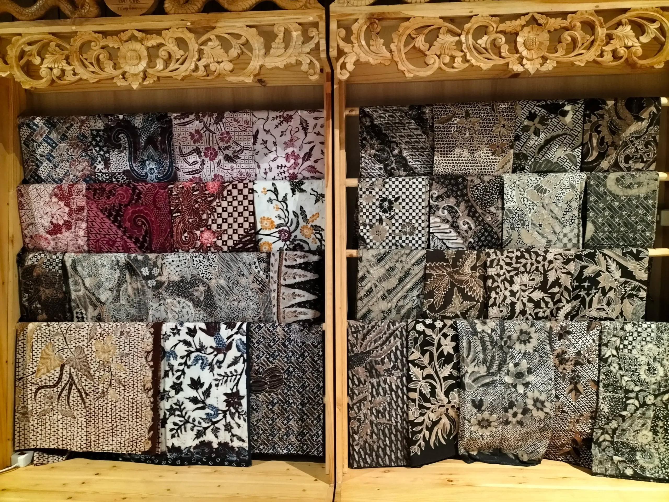 Batik fabric collection displayed on wooden shelves.