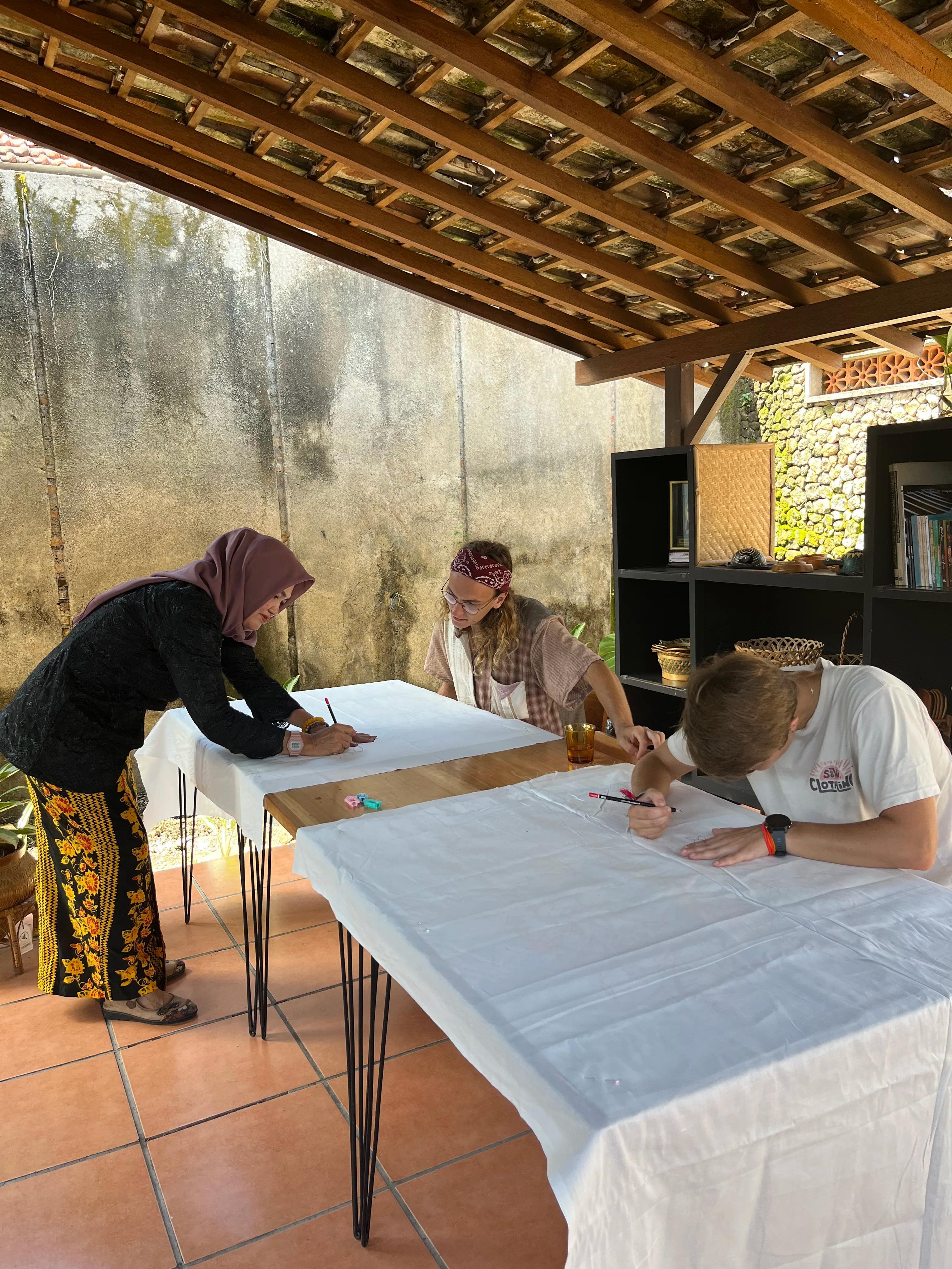Bu Umi assisting a workshop participant with sketching a batik design onto fabric before the canting process